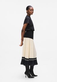 Black t-shirt, ivory pleated skirt with a black hem and white text, glossy black high-heeled boots, smooth texture, side profile view.