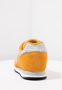 Basket jaune en daim avec des accents gris, vue arrière mettant en valeur le logo et la texture douce, avec une semelle en caoutchouc noir et une semelle intermédiaire blanche.