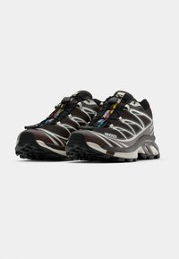 Brūnas un pelēkas sporta kurpes ar melnu zoli, teksturētu augšu un atstarojjošām akcentiem. Aprīkotas ar ātru sašūšanas sistēmu un mīkstinātu dizainu.