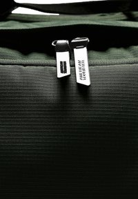 Zaino verde scuro in tessuto con superficie testurizzata; due cerniere argentate contrassegnate "American Tourister" su sfondo verde scuro.