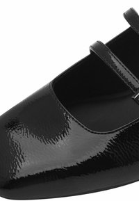 Chaussure Mary Jane en cuir verni noir avec deux fines lanières et un bout arrondi, présentée en gros plan sous un angle.