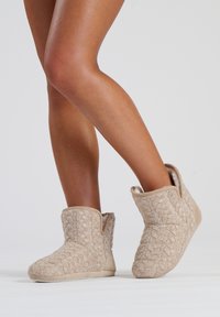 Botines de punto beige hasta el tobillo con un patrón texturizado y un suave forro interior, que presentan un tacón bajo y una suela flexible.