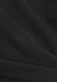 Gros plan sur un tissu noir à texture finement tricotée avec des plis doux créant des variations subtiles d'ombre.
