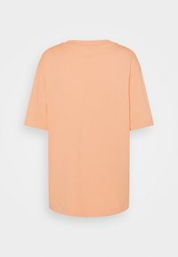 T-shirt oversize à manches courtes couleur pêche avec un col rond, vu de dos sur un fond gris clair uni.