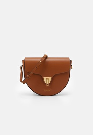 Sac bandoulière en cuir brun en demi-lune avec sangle ajustable, fermoir doré, et logo "COCCINELLE" embossé centré à l'avant.