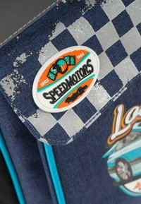 Tessuto a quadretti blu con una superficie testurizzata, caratterizzato da un'etichetta rotonda arancione, nera e turchese con il testo "SPEEDMOTORS."