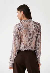 Průhledná blůza s dlouhým rukávem v pastelovém leopardím potisku s jemně fialovými, béžovými a hnědými odstíny; má sklápěcí límec a krajkové detaily na manžetách.