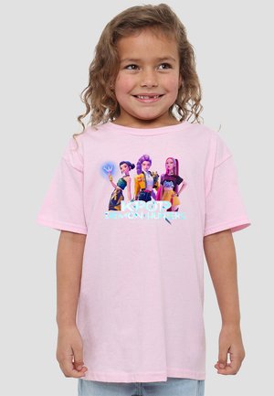 Young girl with curly hair smiling, wearing a light pink T-shirt featuring three animated female characters and "K-POP DEMON HUNTERS" text.
