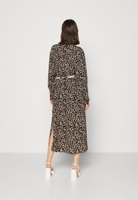 Robe maxi noire à motifs floraux, manches longues, fente sur le côté, ceinture avec logo blanc, tissu léger avec un motif floral varié.