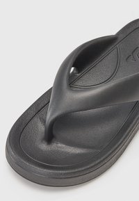 Svart gummiflip-flop med teksturert fotseng, V-formet stripe og en glatt, buet såle for komfort og stabilitet.