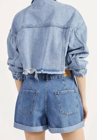 Veste en denim bleu clair au design court avec un ourlet effiloché, associée à un short en denim taille haute assorti avec deux poches arrière.