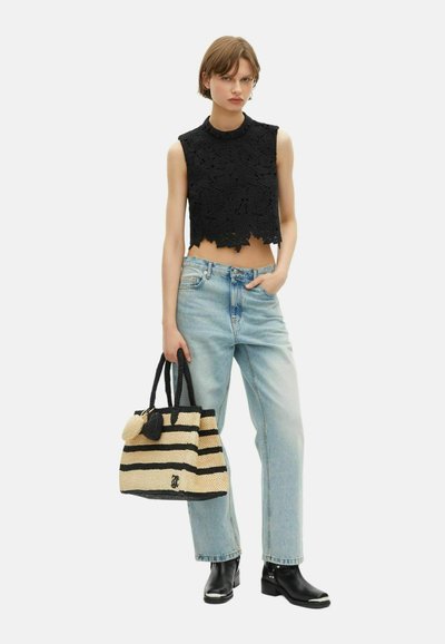 Frau trägt ein schwarzes, Blumenspitze, ärmelloses Crop-Top, hellblaue High-Waist-Jeans, schwarze Stiefel und hält eine gestreifte, gewebte Tragetasche.