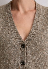 Brązowy dziany kardigan z dekoltem w serek, wykonany z fakturowanego materiału, z dwoma ciemnymi guzikami i cętkami w różnych kolorach na całej powierzchni.