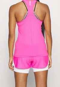Kvinna sedd bakifrån, iklädd en rosa atletisk linne, rosa shorts med vita underställ och en lila Under Armour sport-bh.