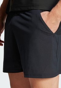 Schwarze Sportshorts aus strukturiertem Stoff, ausgestattet mit seitlichen Taschen und einer lockeren Passform. Der Bund ist elastisch für zusätzlichen Komfort.