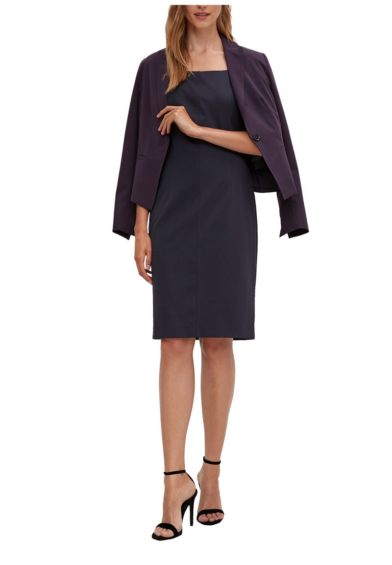 Dunkelblaues Kleid mit taillierter Silhouette, quadratischem Ausschnitt und passender, kurz geschnittener Blazer. Schlanke schwarze Riemchen-Heels runden den Look ab.