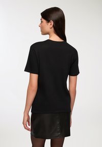 Czarny bawełniany t-shirt z klasycznym okrągłym dekoltem i krótkimi rękawami. Materiał jest gładki, z luźnym krojem i bez widocznych grafik.