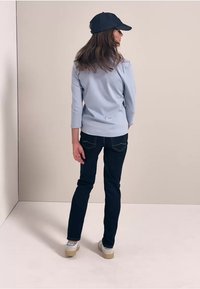 Jasnoniebieska koszula z długim rękawem, ciemne dopasowane dżinsy i granatowa czapka. Casualowe obuwie z beżowymi podeszwami. Prosty design, czyste linie i stonowane kolory.