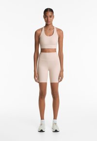 Nude sportoutfit met een halter sportbh en high-waisted shorts. Soepele textuur, minimalistisch ontwerp en een getailleerde silhouet.