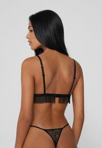Černá souprava spodního prádla se síťovaným skládáním na zadním pásu a krajkovými tanga. Nastavitelné ramínka a složitý krajkový vzor na tanga.