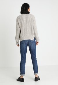 Beżowy sweter z dzianiny z teksturowanym wzorem, ściągaczami na mankietach i dole. Połączony z niebieskimi jeansami z podwiniętymi nogawkami i czarnymi butami. Prosty, casualowy styl.