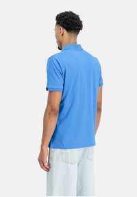 Zila polo krekls ar apkakli un īsām piedurknēm, izgatavots no gludas auduma. Tam ir logotips uz kreisās piedurknes un taisna apakšdaļa.