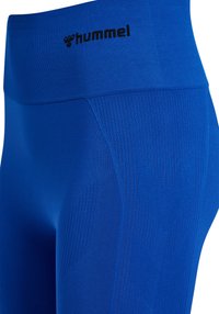 Blå leggings lavet af elastisk materiale med en ribstrikket linning, med en logo og teksturerede mønstre på siderne.