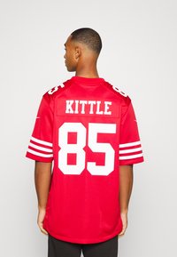 PirosFootball mez fehér csíkkal az ujjakon, "KITTLE" névvel és "85" számmal feltüntetve a hátulján vastag fehér betűkkel.