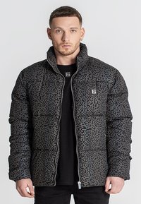 Puffjakke i sort med et pixelmønster, der har en lynlås lukning og en oprejst krave. Blødt, quiltet tekstur med skjulte lommer.