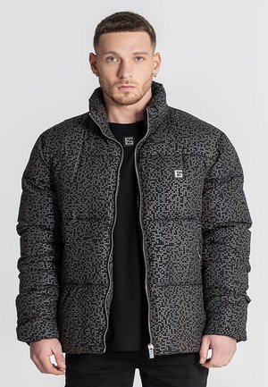 Chaqueta de plumas en negro con un patrón pixelado, que cuenta con un cierre de cremallera y un cuello alto. Textura suave y acolchada con bolsillos ocultos.