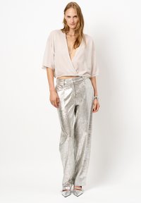 Lichtbeige cropped top met een diepe V-hals; metallic zilveren wijdtemottige broek met een glanzende textuur; puntige metallic schoenen.