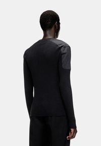 Pull noir à côtes avec des accents en cuir sur les épaules, offrant une coupe ajustée et des manches longues, vu de dos.