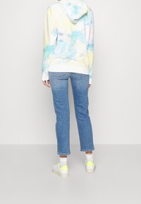 Felpa tie-dye pastello con tasca a marsupio bianca, abbinata a jeans dritti azzurri chiari e sneaker bianche con dettagli giallo neon.