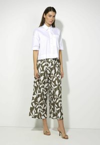 White cropped button-up shirt with short sleeves, paired with olive green wide-leg pants featuring a white leaf pattern. Tan heeled sandals.