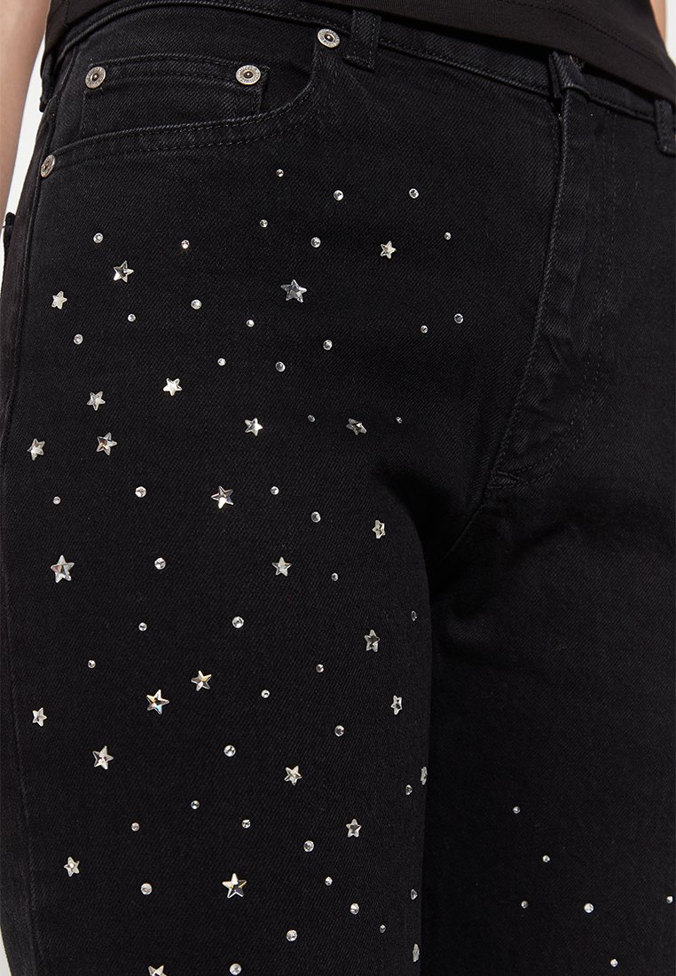 Schwarze Jeans aus Denim mit verstreuten silbernen Sternen und Strassverzierungen über dem Stoff, die ein strukturiertes Design hervorheben.