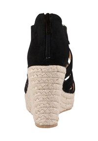 Sandale compensée en suède noir avec une plateforme en jute tissé, talon découvert et fermeture éclair à l'arrière. Présente un design avec des découpes sur les côtés pour la ventilation.