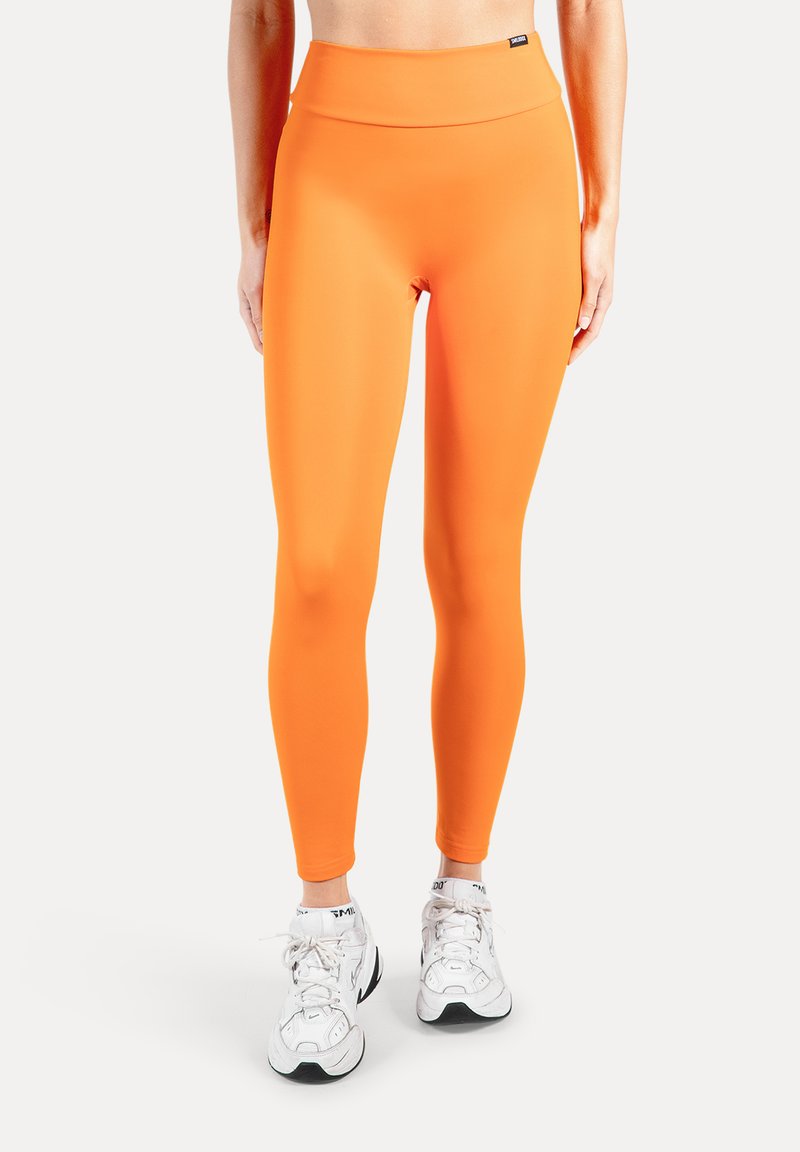 Oranje leggings van een soepel, rekbaar materiaal. Hoge tailleband en een volledige lengte, gecombineerd met witte sportschoenen.