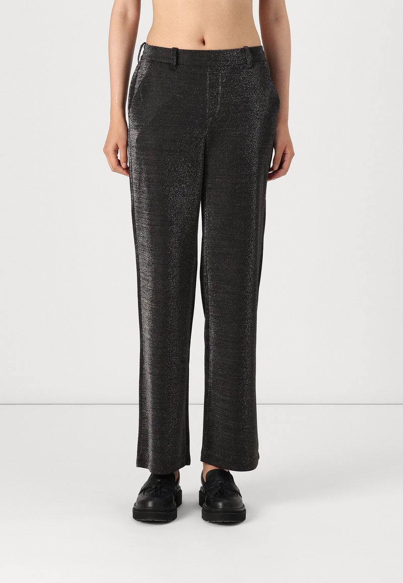 Pantalons noirs taille haute avec une surface texturée et scintillante, dotés de poches latérales et d'une coupe droite. Portés avec des chaussures noires.