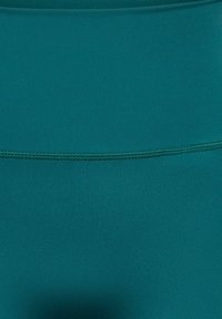 Gros plan sur un tissu bleu sarcelle avec une couture horizontale visible traversant le centre.