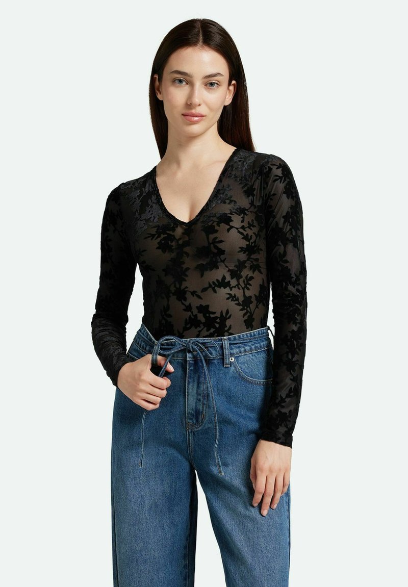 Schwarzer Langarm-Body mit floralem Spitzenmuster und tiefem V-Ausschnitt, kombiniert mit hochgeschnittenen blauen Jeans.