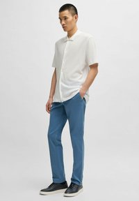 Short-sleeve white textured shirt, blue pants, and black sneakers. Notable button details on the shirt and slim-fit pant design.