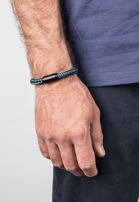 Mustard ja teeritud käevõru koos sujuva silindrilise musta aksessuaari tükiga, kantud randmel neutraalse tausta against.