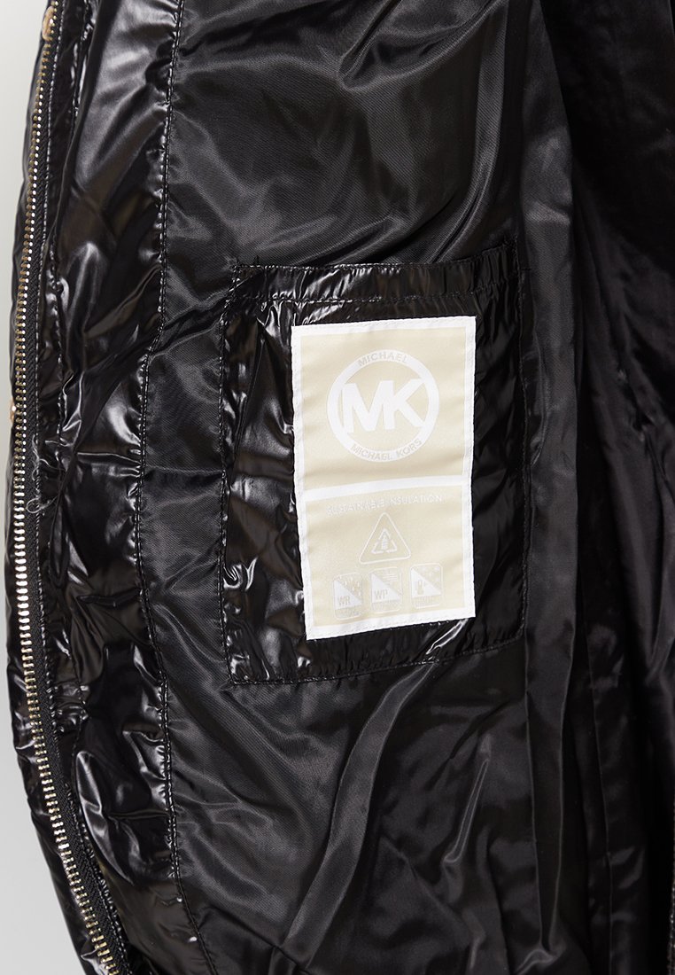 Interno di un giubbotto trapuntato nero con una texture liscia e lucida. Presenta un'etichetta con il logo "MK" e simboli di cura su uno sfondo beige.