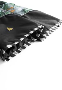 Sort stof med en glat tekstur, der har en farverig topsektion med naturmotiver, et guldlogo og en stribet kant.