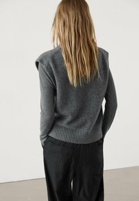 Harmaa neulottu villapaita, jossa on ribattu helma ja olka yksityiskohta, yhdistettynä mustiin raidallisiin housuihin. Pehmeä rakenne, rento istuvuus.