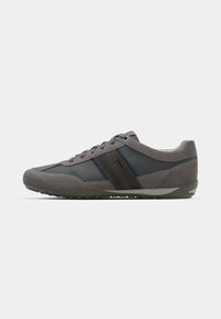 Zapatilla deportiva gris que combina materiales de ante y malla. Diseño único con rayas oscuras en contraste, suela de goma y cierre con cordones.