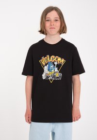 Camiseta de algodón negra con un gráfico colorido que presenta el texto "VOLCOM", un coche de dibujos animados y un personaje azul sobre un fondo blanco.