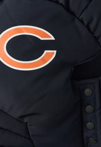 Σκούρο μπλε μπουφάν puffer με πορτοκαλί και λευκό λογότυπο "C". Διαθέτει καπιτονέ υφή και μαύρα κουμπιά τύπου snap στο πλάι για κλείσιμο.