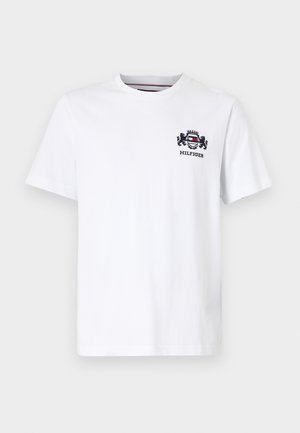 T-shirt bianco in cotone a maniche corte, con un design del logo blu navy e rosso sul lato sinistro del petto. Collo rotondo, texture liscia.