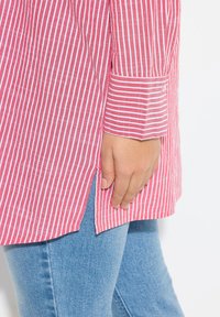 Camicia a righe rosse e bianche con colletto button-down, maniche lunghe e orlo arrotondato, abbinata a jeans blu chiaro.